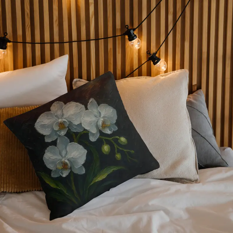 White orchid impasto pillow on neutral bedding, glowing white blooms with icy blue highlights and gold shimmer